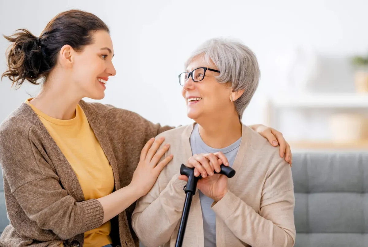 A support worker with an arm around a smiling older woman holding a walking cane